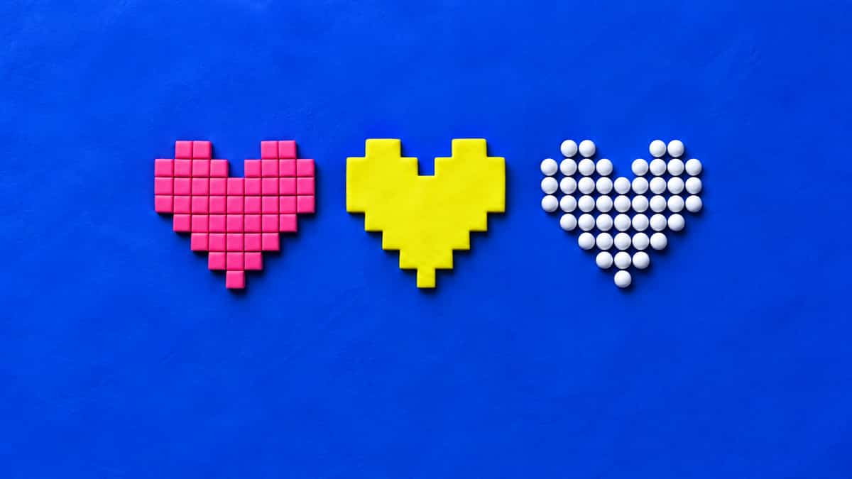 Three pixel hearts on blue clay: a mosaic of separate pink square tiles, a yellow stepped heart cut from one slab, and a heart of round white clay beads.