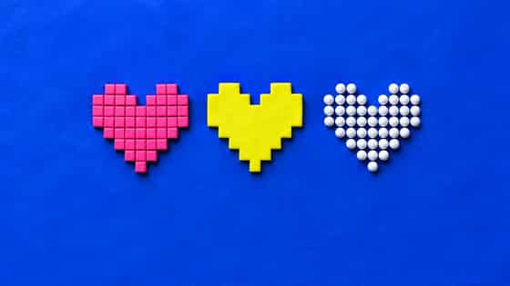 Three pixel hearts on blue clay: a mosaic of separate pink square tiles, a yellow stepped heart cut from one slab, and a heart of round white clay beads.