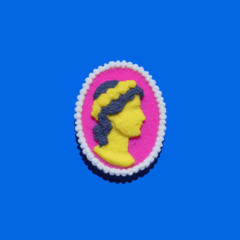 Oval polymer clay cameo brooch on a bright blue background: a raised yellow classical profile looking right with slate navy hair and a yellow band, on a fuchsia oval framed by whi…