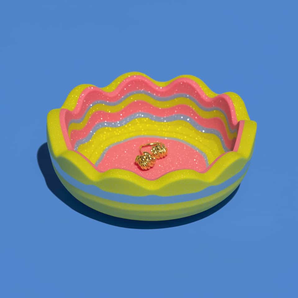 Sparkly polymer clay ring dish with a wavy rim, nested wavy bands of yellow and pink with thin blue lines inside down to a pink floor, and a yellow outside with a blue stripe, hol…