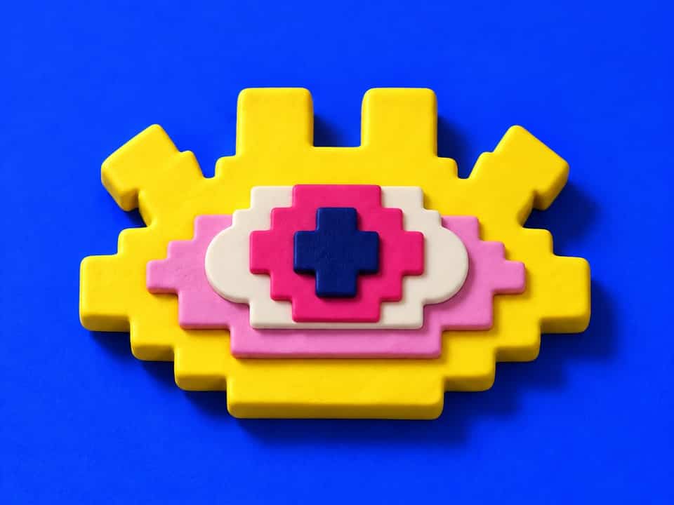 A layered Pixel Eye made from five cut clay shapes: yellow base, light pink backing, white, pink iris and dark blue pupil.