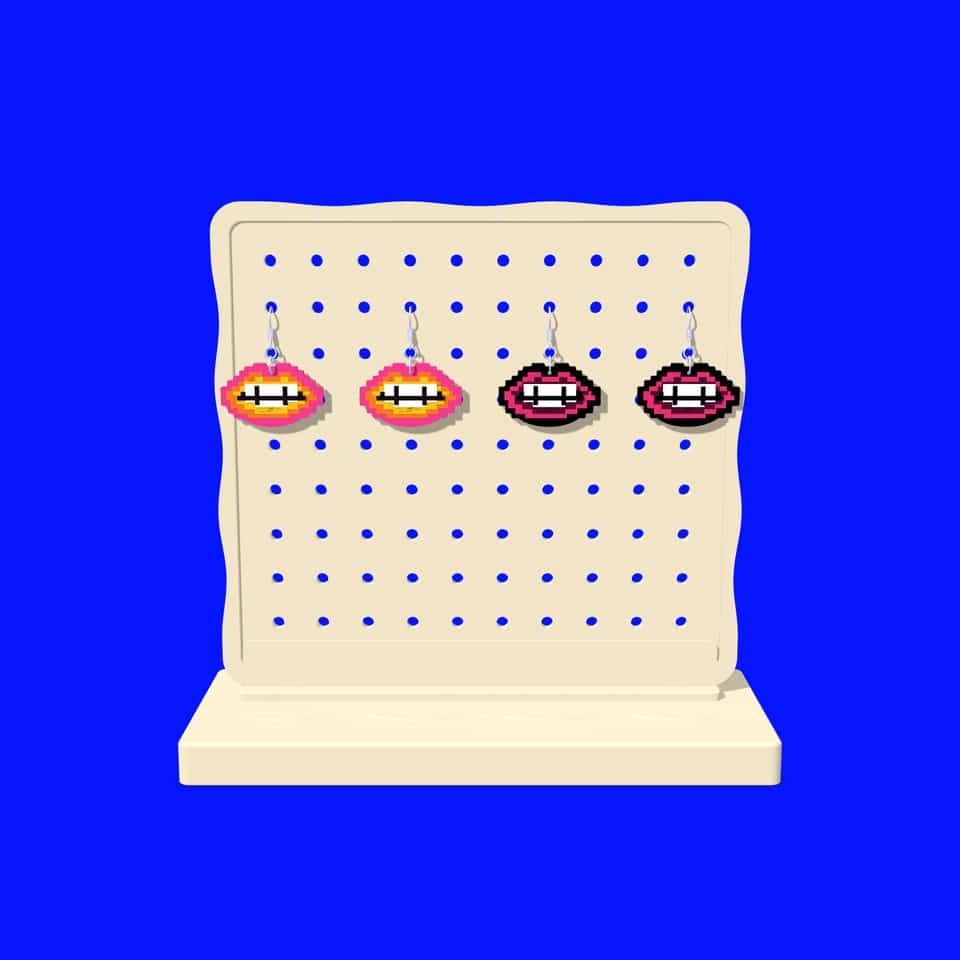 Two pairs of 44 mm Pixel Lips drop earrings, in the kit colours and Classic Kiss, hanging from the printed pegboard of the display stand. The 44 mm drops are about 5.3 g per earring with findings; weigh your pair.