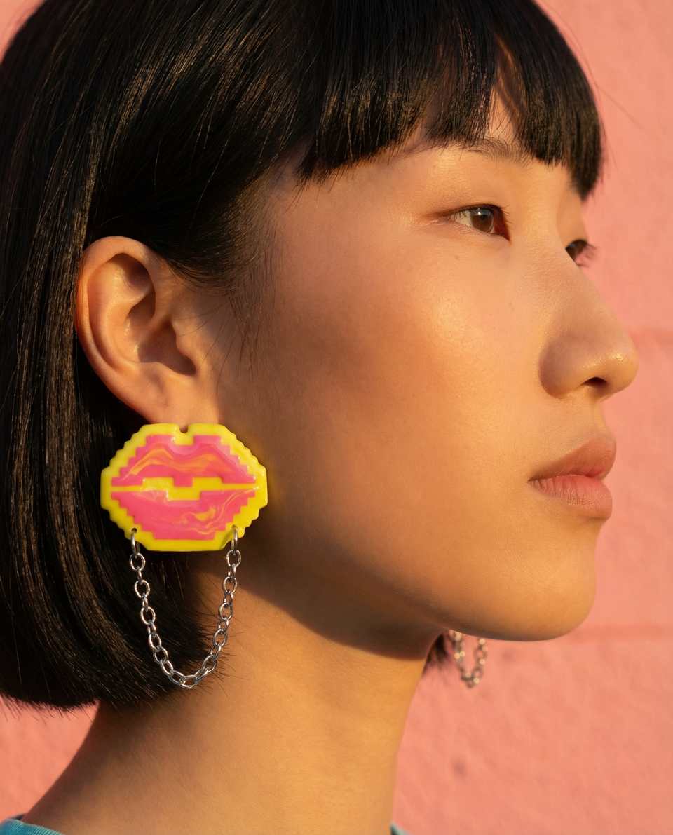 Pink pixel lips earring with chain detail worn in profile against pink background