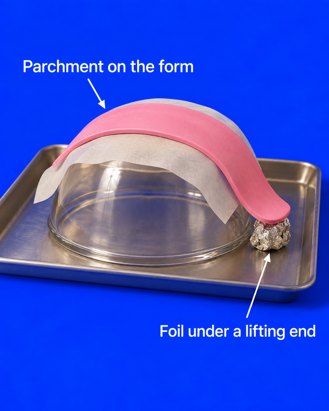 A curved pink clay collar rests on parchment over an upturned oven-safe glass bowl on a baking tray, with a small foil support under its lifting end.