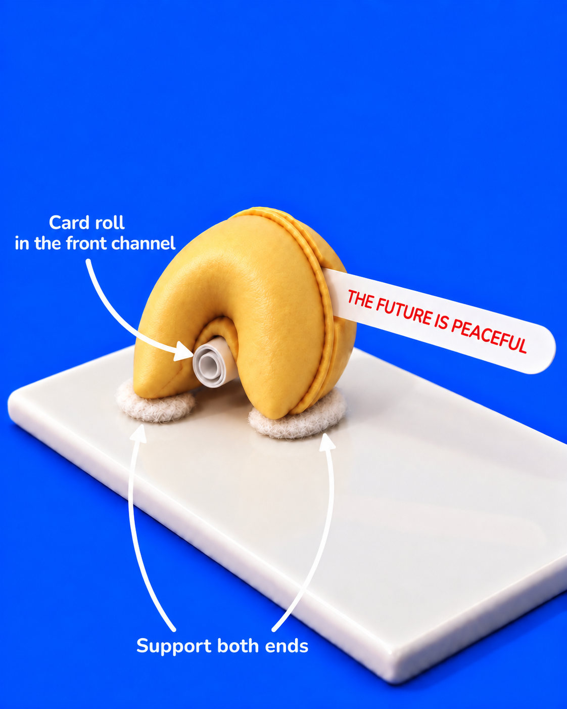A white card roll supports the front channel of a folded clay fortune cookie while a separate lettered message leaves the high side mouth; fiberfill cradles both rounded ends.