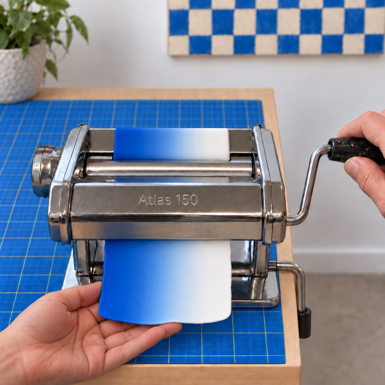 A clay sheet emerging from beneath the rollers of a pasta machine, shading from deep blue on the left through pale blue to white on the right.